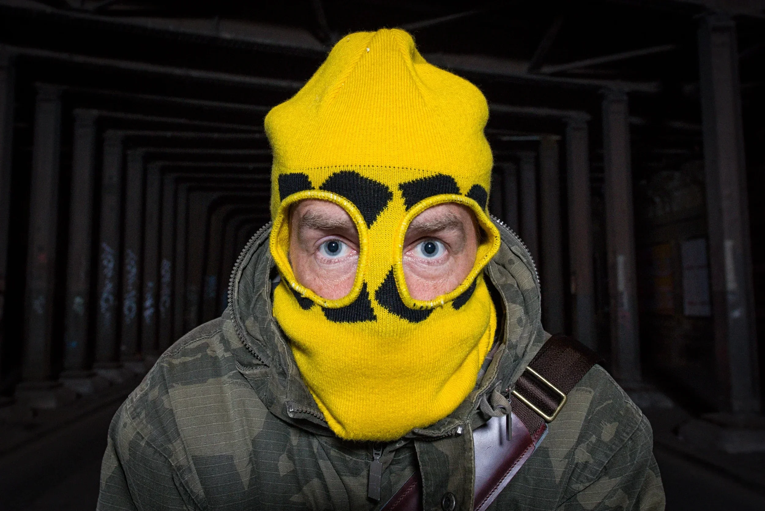Intense close-up portrait of the cyclist wearing a yellow and black patterned balaclava.